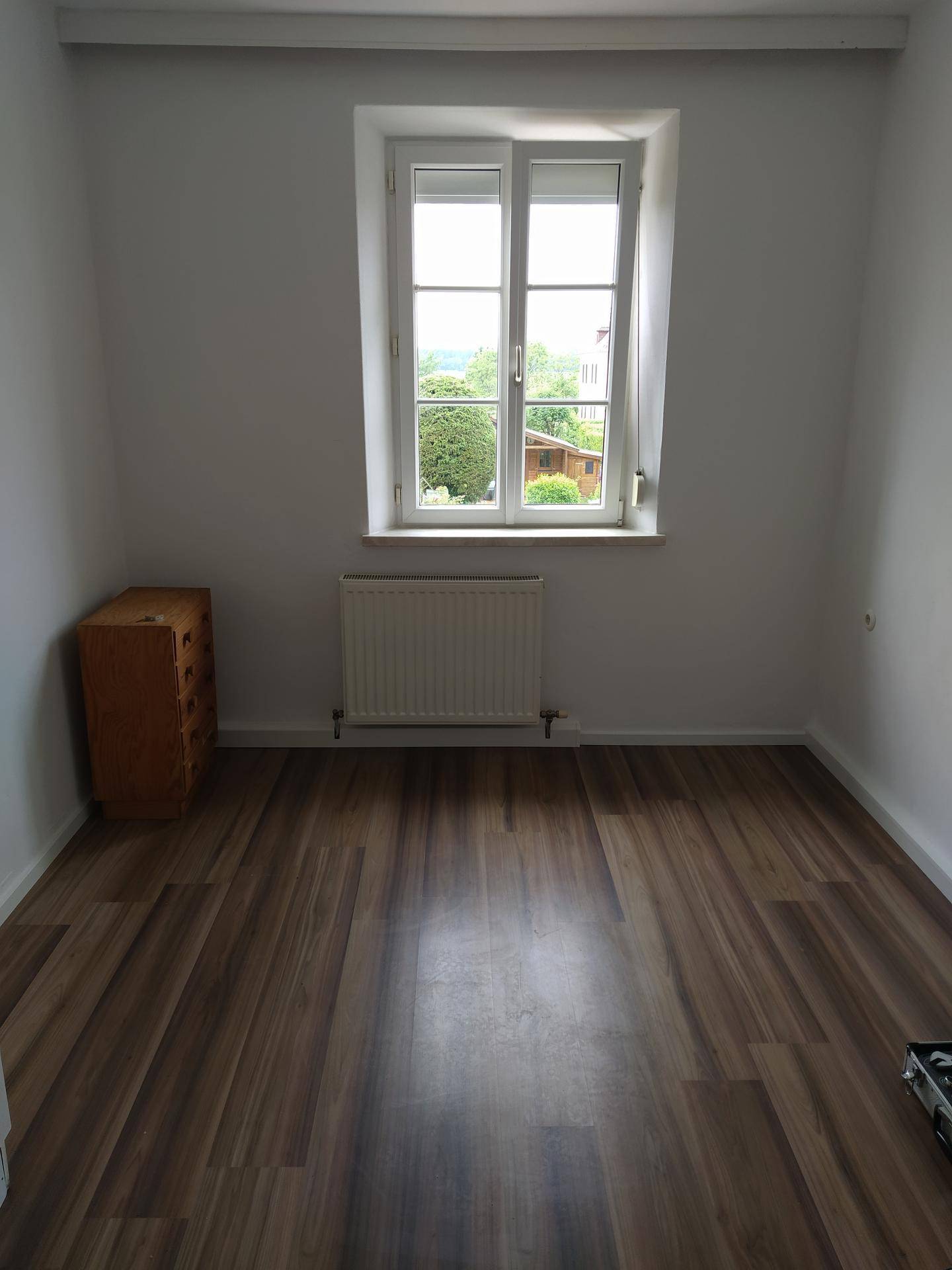 Helles Zimmer mit Laminatboden, einem Fenster und einem angenehmen Blick ins Grüne.