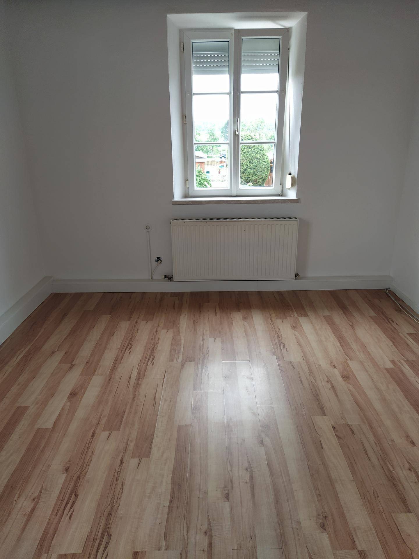 Freundliches Zimmer mit Laminatboden, Heizkörper und Fenster mit Außenjalousien für Privatsphäre.