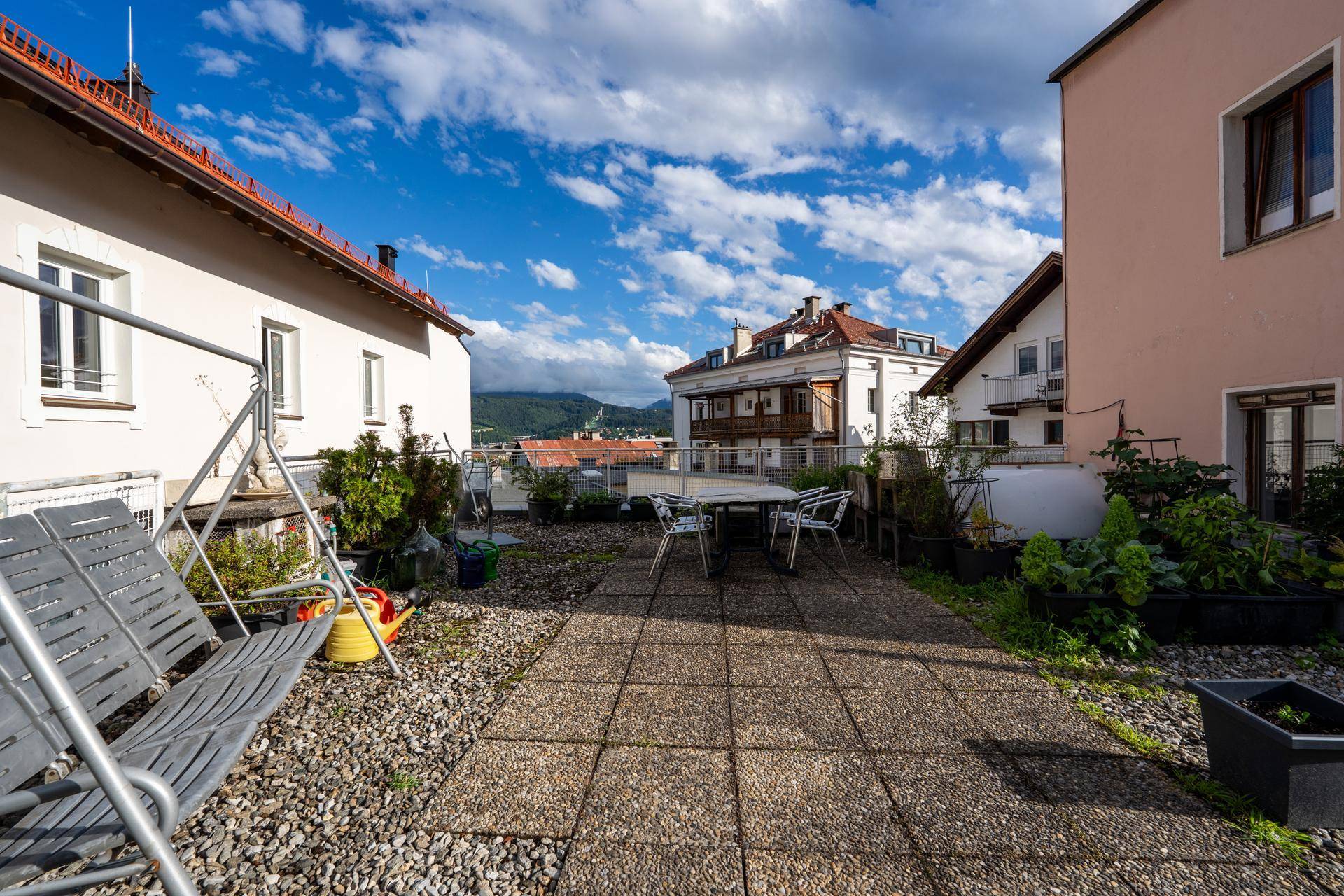 Weitläufige Dachterrasse mit Sitzgelegenheiten, Schaukel und Blick auf die umliegenden Gebäude und Berge.