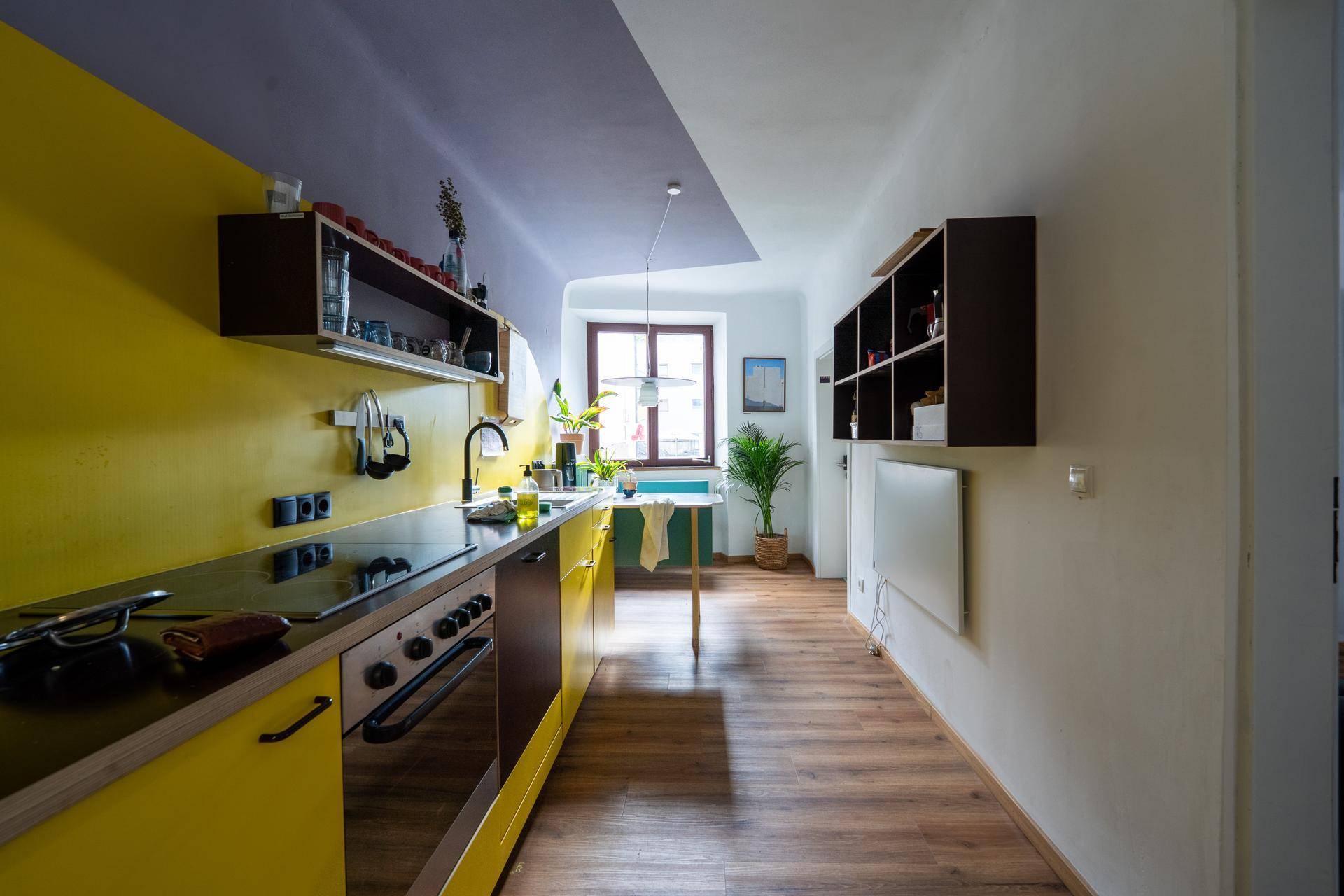 Moderne Küche mit gelben und braunen Fronten, Holzboden und einem Fenster, das viel Licht hereinlässt.