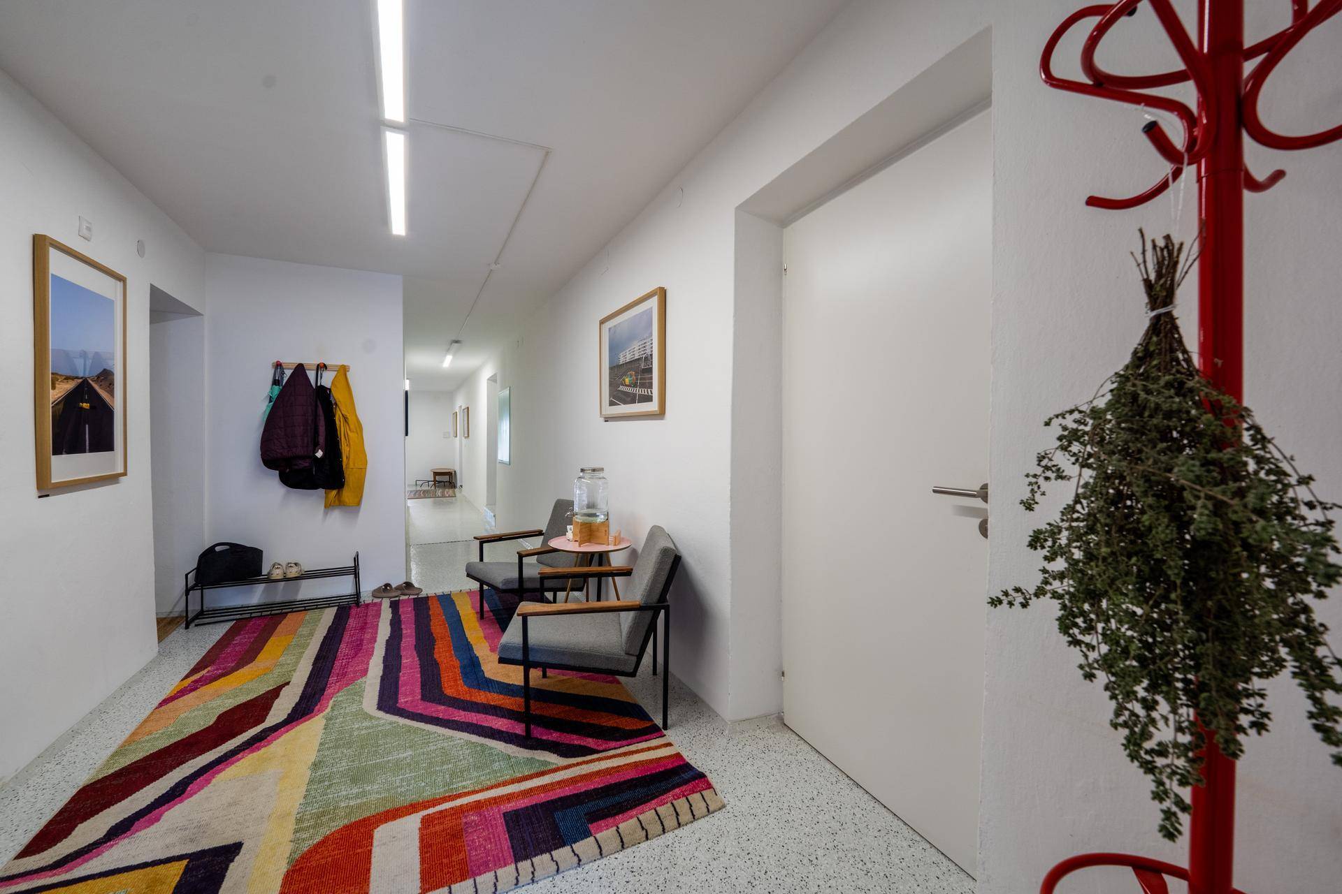 Langer, heller Flur mit bunter Teppichläufer, Garderobe und Blick in den hinteren Bereich.