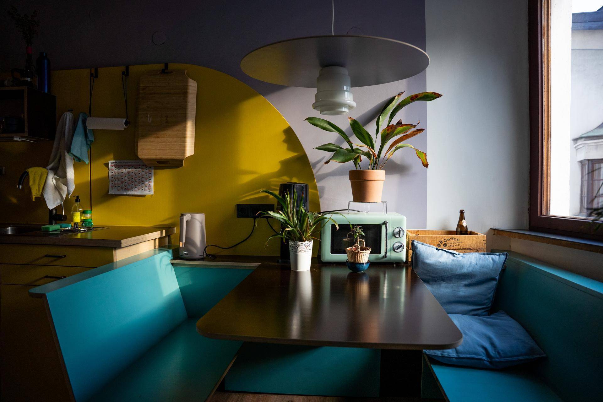 Gemütliche Küchenzeile mit integrierter Sitzecke, Mikrowelle und farbigen Wänden, ideal für kleine Mahlzeiten.