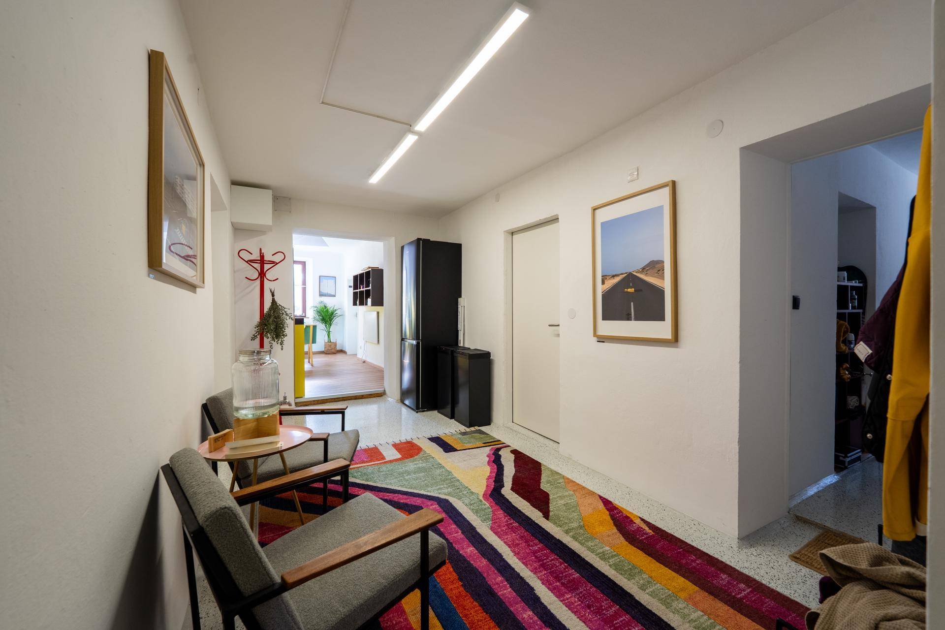 Freundlicher Eingangsbereich mit bunter Teppichläufer, Sitzgelegenheiten und Garderobe, führt zu weiteren Räumen.