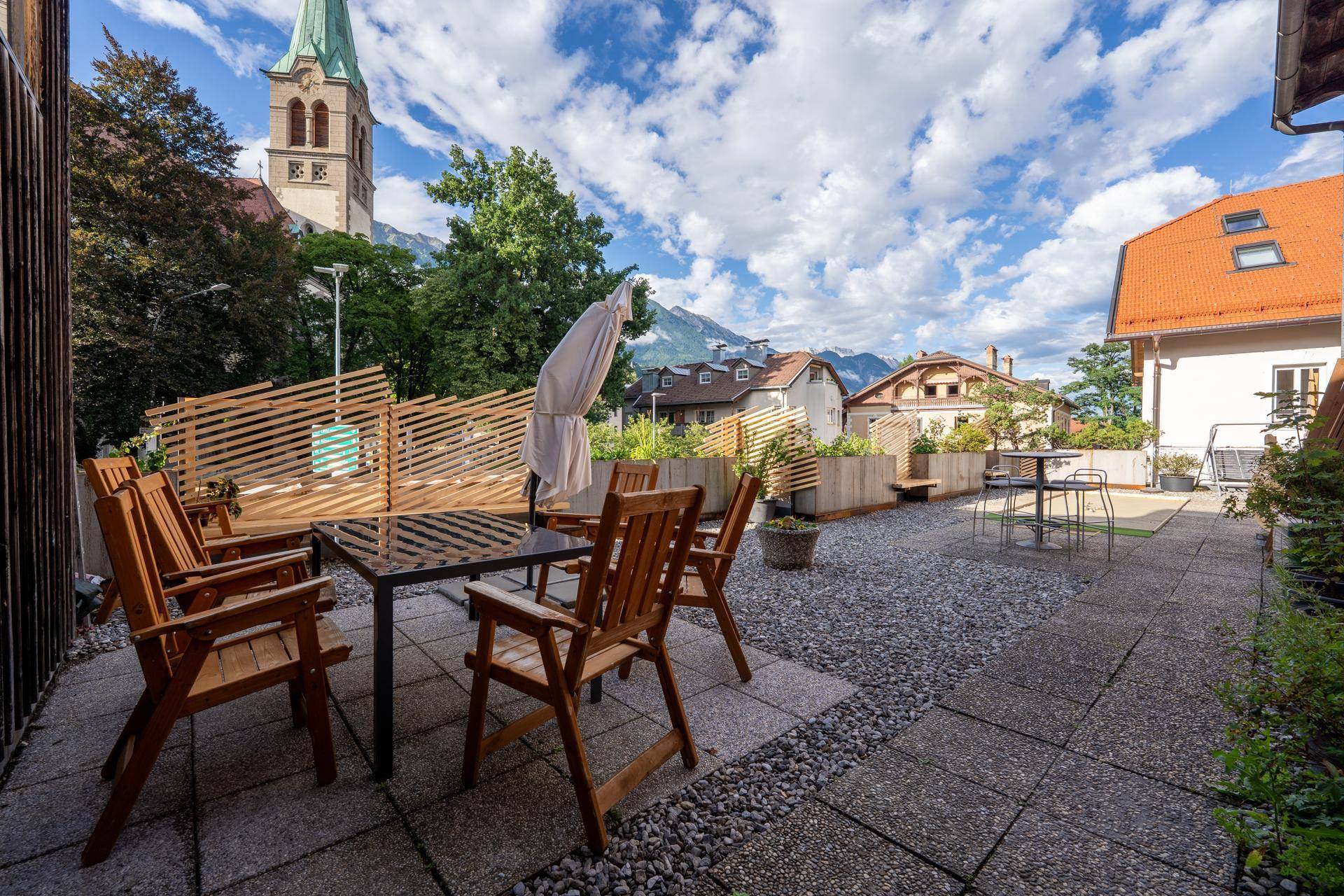 Große Dachterrasse mit Sitzgelegenheiten, Kies und Plattenboden, umgeben von Holzzäunen und Bergblick.