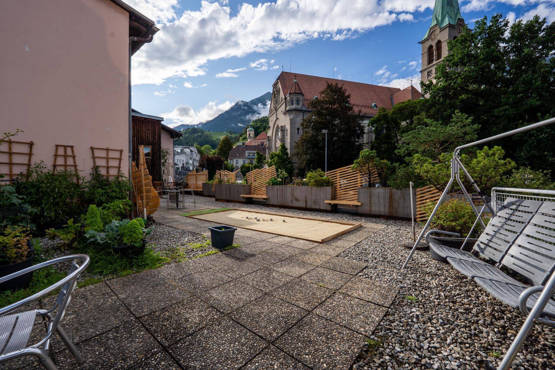 Große Dachterrasse mit Boccia-Bahn, Schaukel und Blick auf die Kirche und die umliegende Berglandschaft.