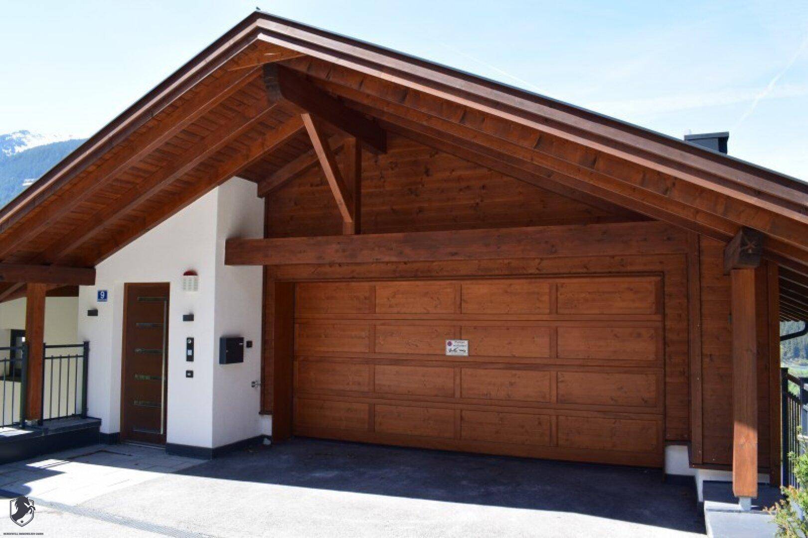 Eingangsbereich und Holzgarage eines modernen Hauses mit traditionellen Holzelementen und Satteldach.