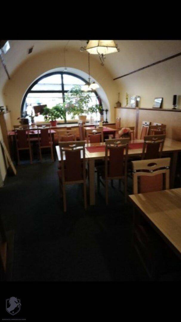 Geräumiger Speisesaal mit Holztischen und Stühlen, beleuchtet durch ein großes Rundbogenfenster.