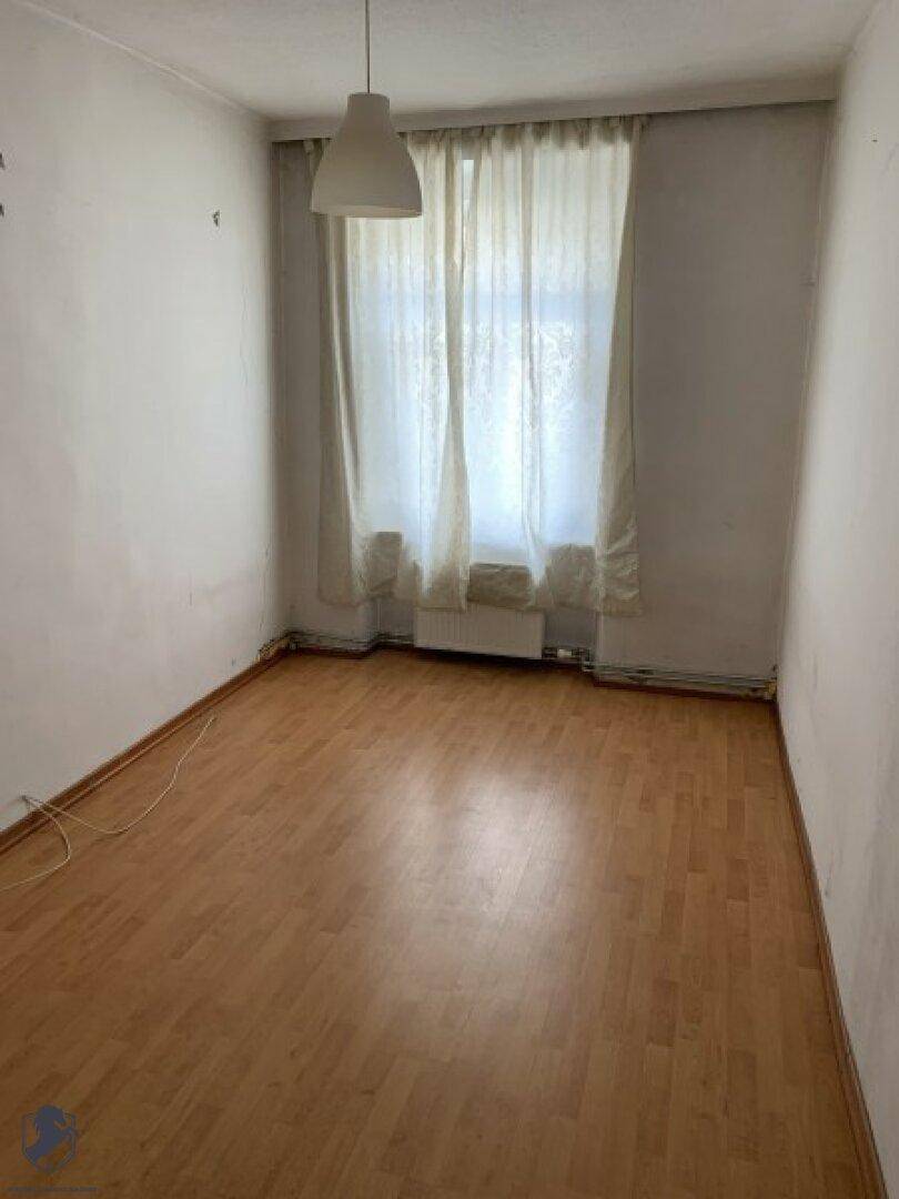Leerer Raum mit Laminatboden und einem Fenster mit hellen Vorhängen.