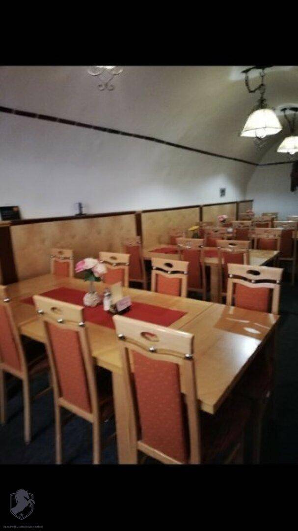 Weitläufiger Speisesaal mit zahlreichen Holztischen und roten Stühlen, bereit für Gäste.