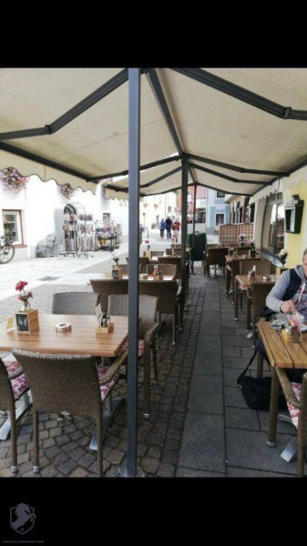 Überdachte Außenterrasse mit Tischen und Stühlen, ideal für Mahlzeiten im Freien.