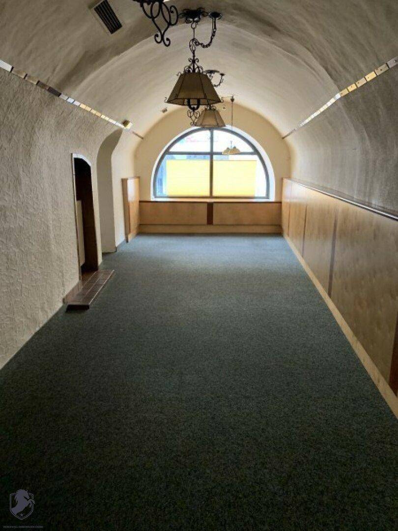 Leerer Raum mit gewölbter Decke, Teppichboden und einem großen Rundbogenfenster.