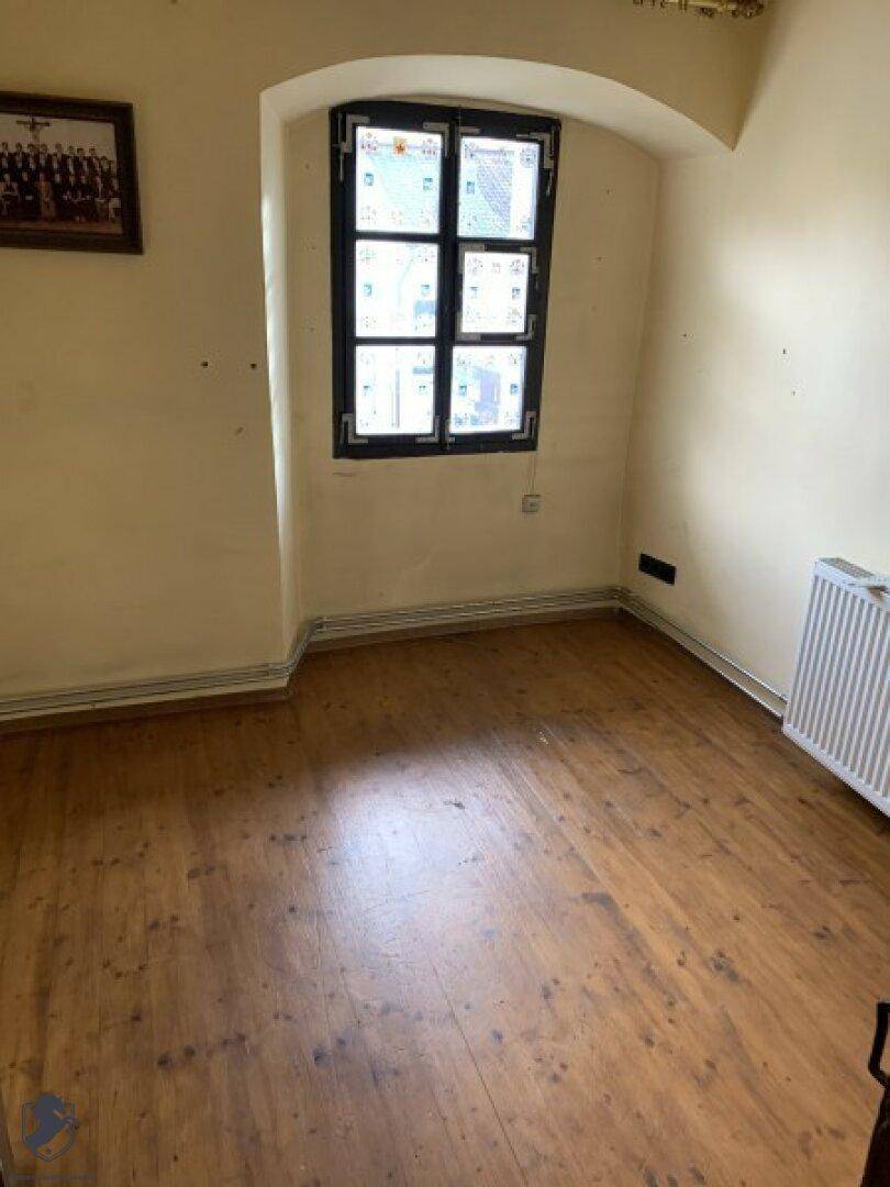 Leerer Raum mit Holzboden und einem Fenster, das Tageslicht hereinlässt.