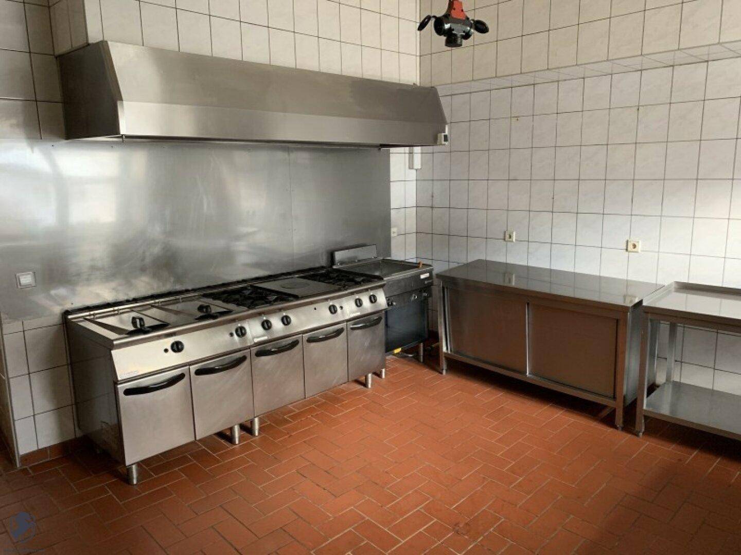 Professionelle Großküche mit Edelstahlgeräten, Gasherd und gefliesten Wänden und Boden.