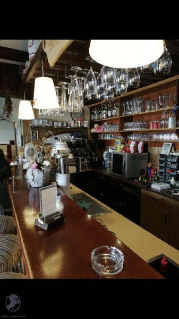 Gut ausgestatteter Barbereich mit Holztheke, Regalen voller Gläser und Flaschen.