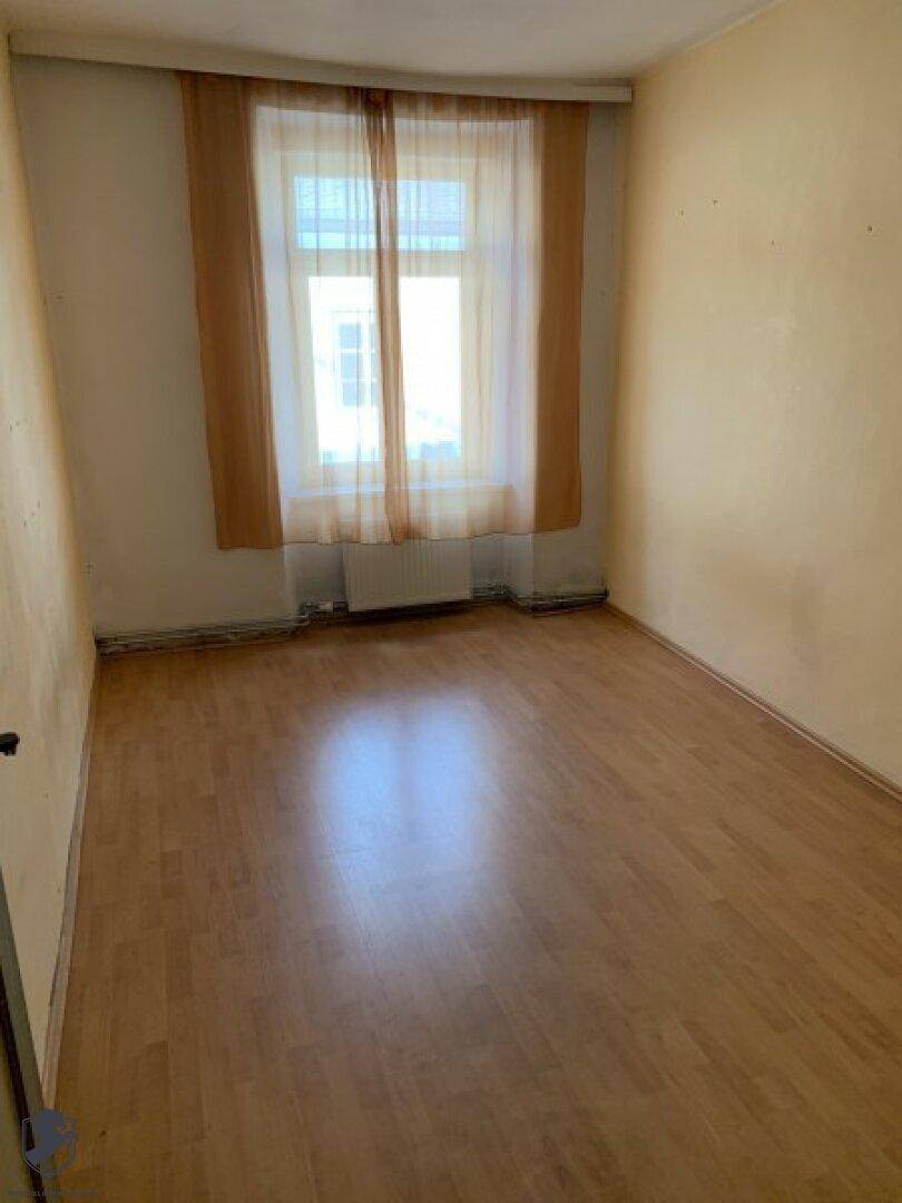 Leerer Raum mit Laminatboden und einem Fenster, das den Raum erhellt.