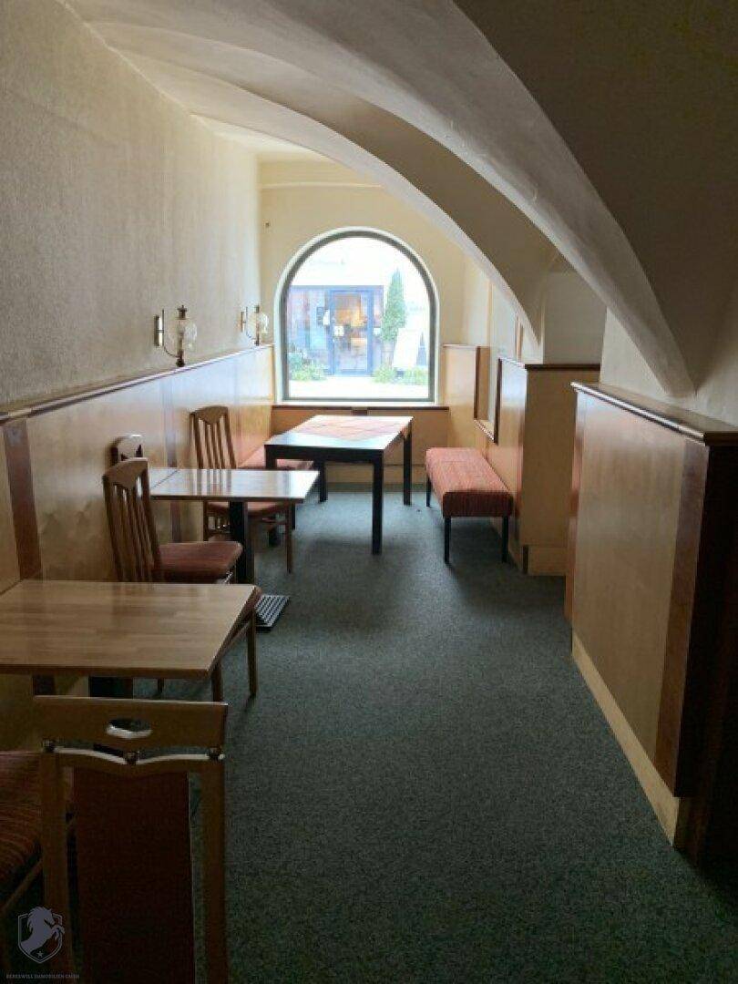 Speisesaal mit Holztischen, Bänken und einer gewölbten Decke, beleuchtet durch ein Rundbogenfenster.