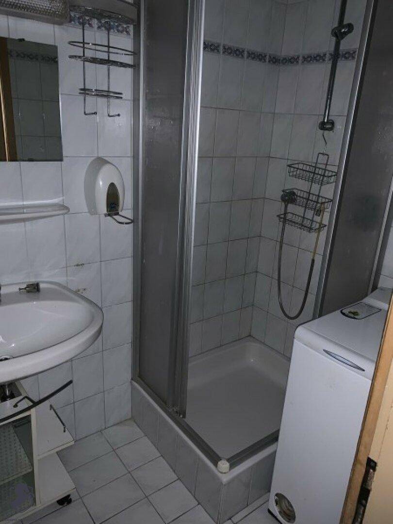 Badezimmer mit Duschkabine, Waschbecken und weißen Fliesen an Wänden und Boden.