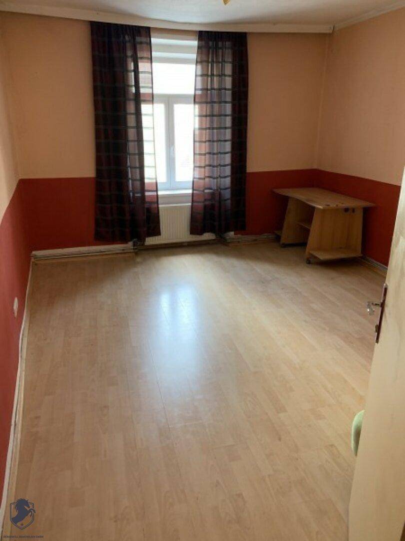 Leerer Raum mit Laminatboden und zweifarbigen Wänden in Rot und Beige.