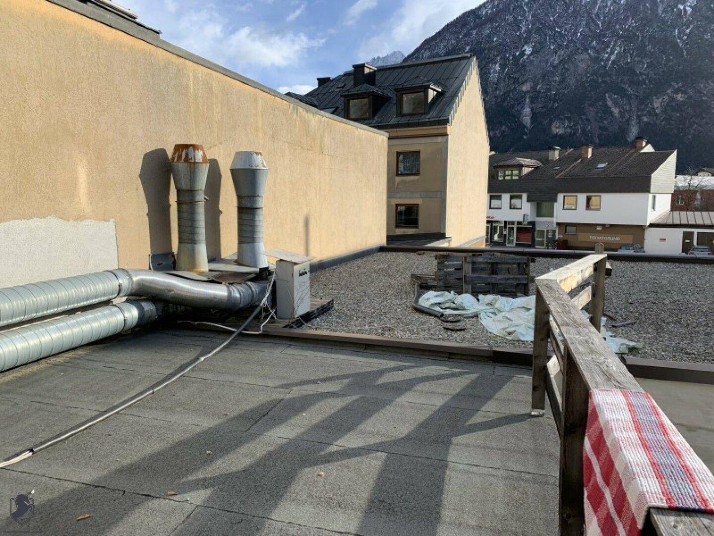 Flachdach mit Lüftungsrohren und Blick auf die umliegenden Gebäude und Berge.