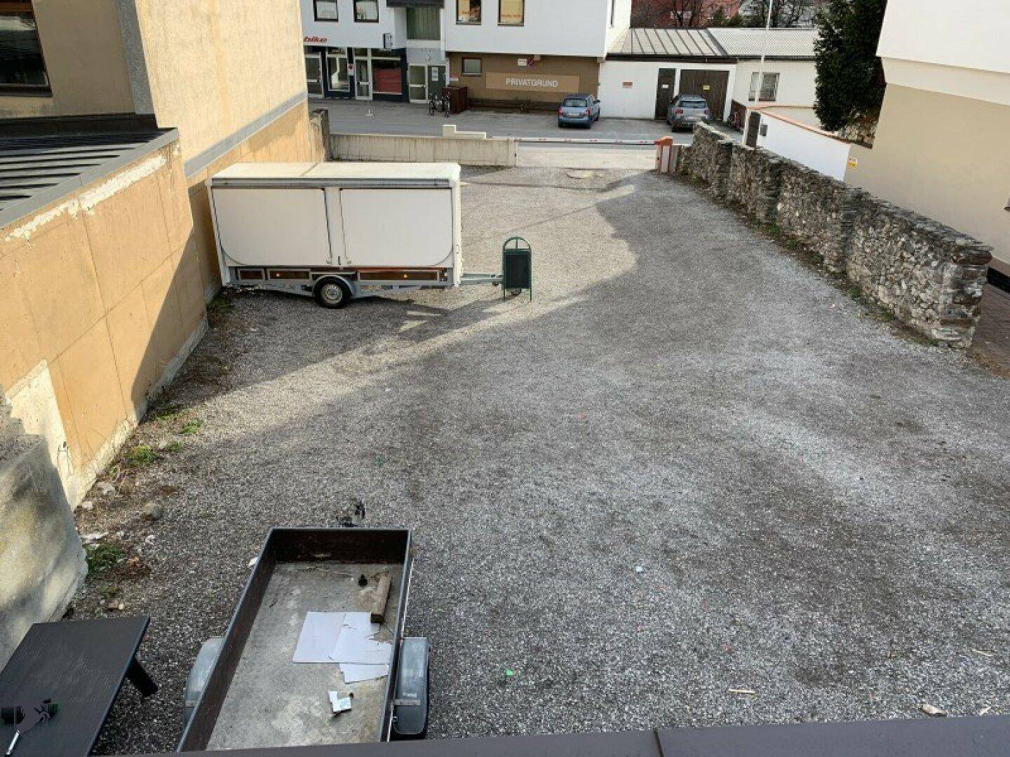 Schotterparkplatz mit einem Anhänger und einer alten Steinmauer im Hintergrund.