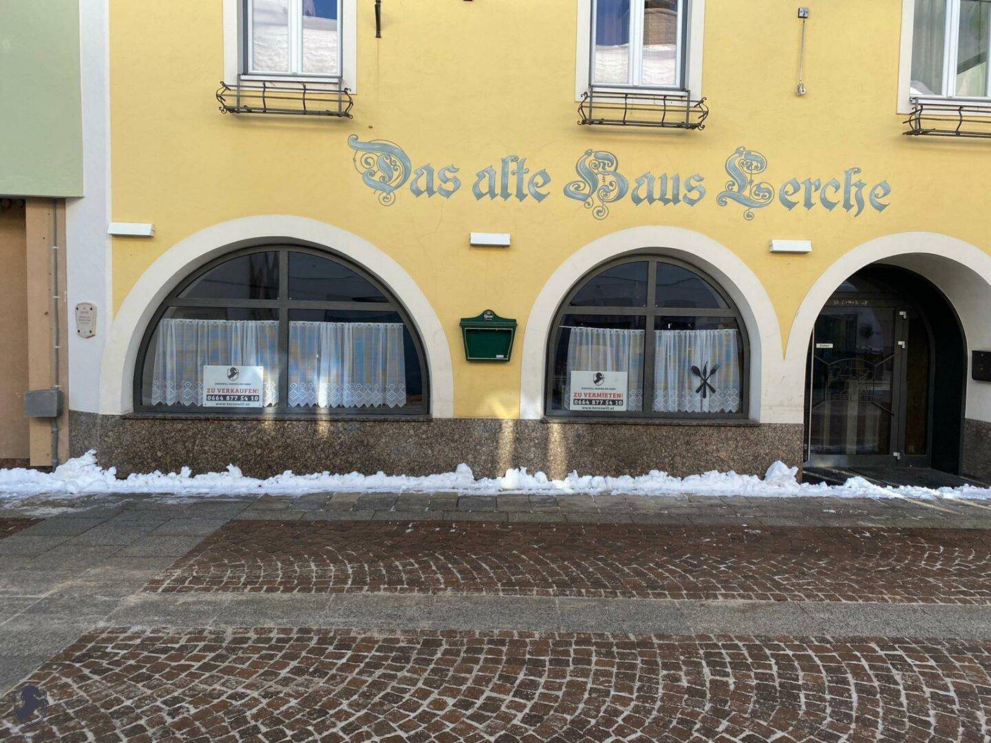 Nahaufnahme der gelben Fassade eines alten Gebäudes mit Rundbogenfenstern und Schneeresten am Sockel.