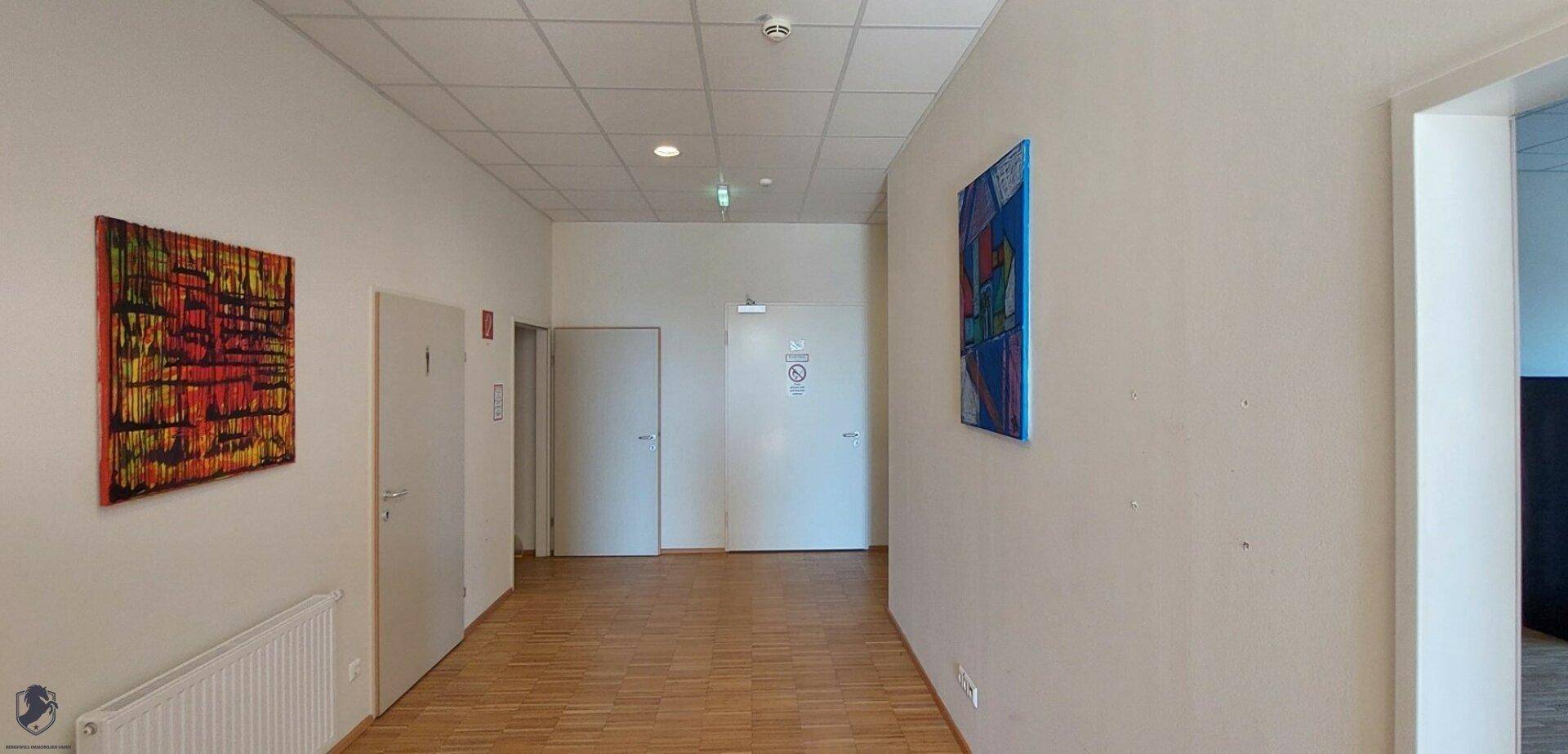 Heller Flur mit weißen Wänden, Holzboden, mehreren Türen und dekorativen Kunstwerken.