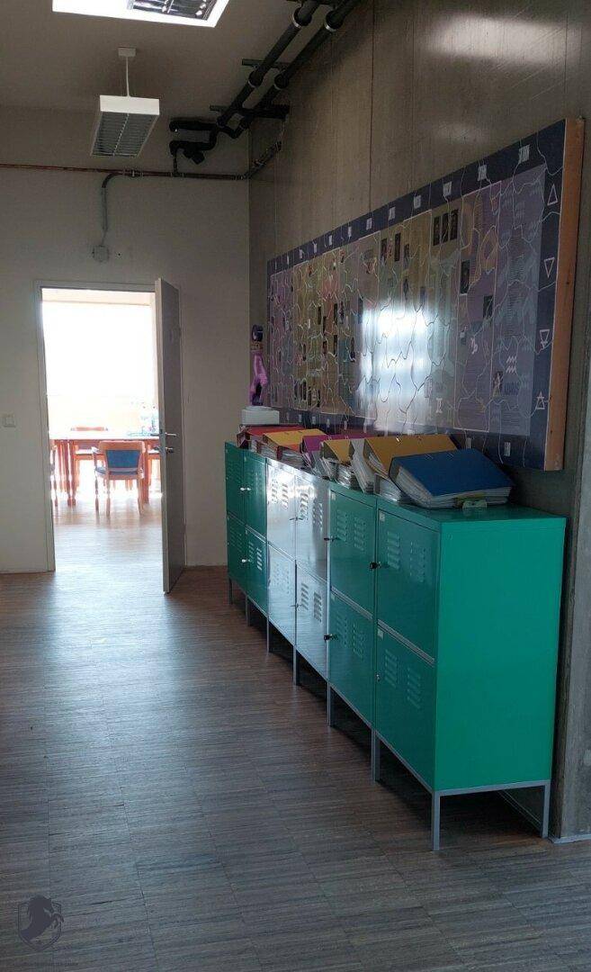Gemeinschaftsbereich oder Flur mit grünen Spinden, einer großen Tafel und Holzboden.