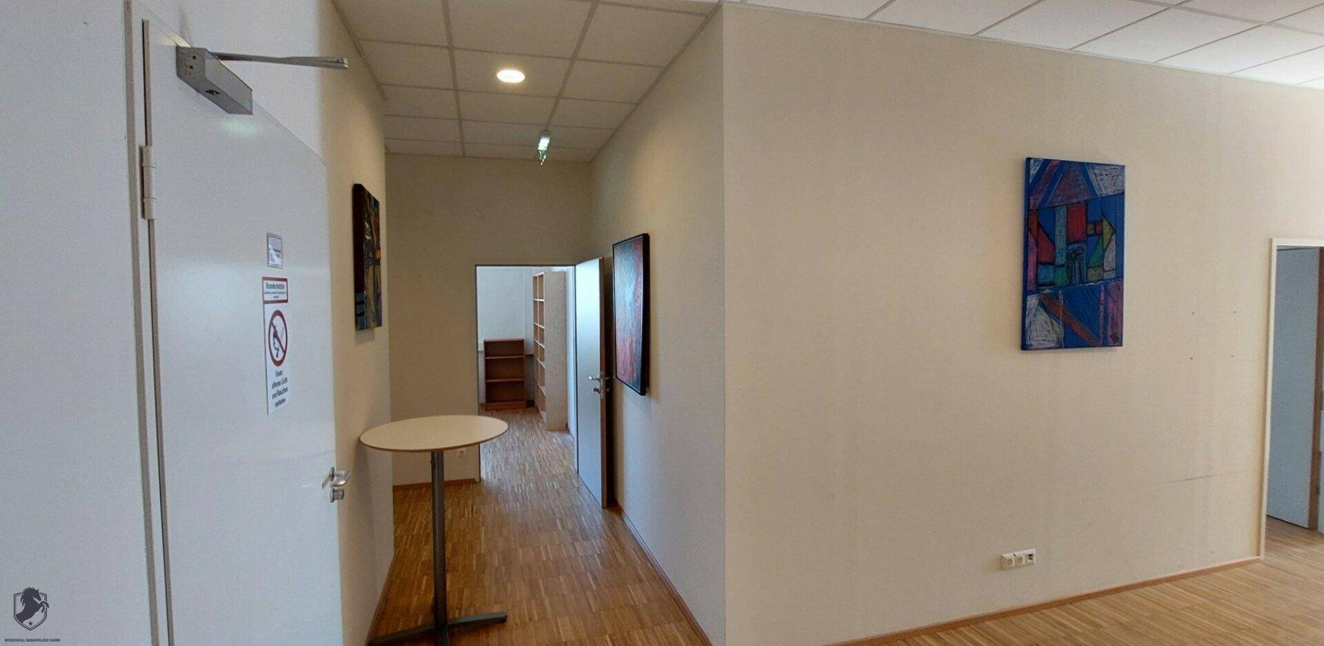 Heller Flur mit weißen Wänden, Holzboden, einem kleinen Stehtisch und moderner Kunst an der Wand.