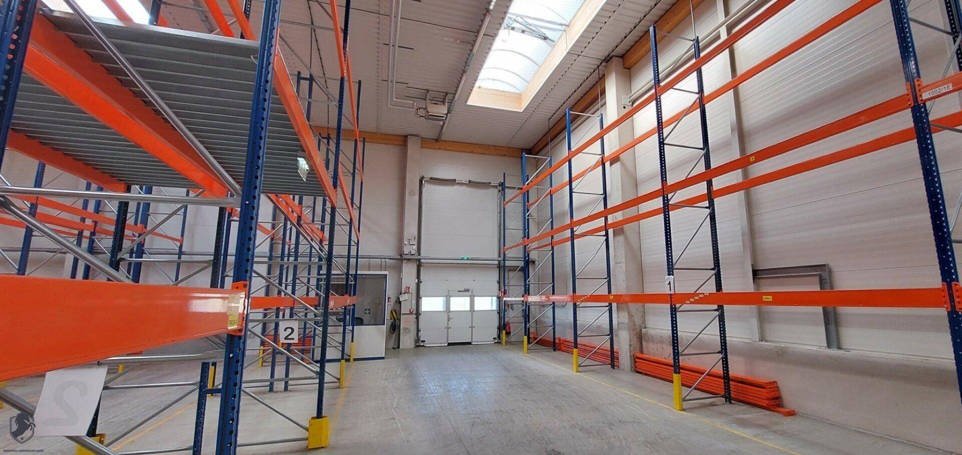 Leere Lagerhalle mit Regalsystemen und einer Laderampe im hinteren Bereich.