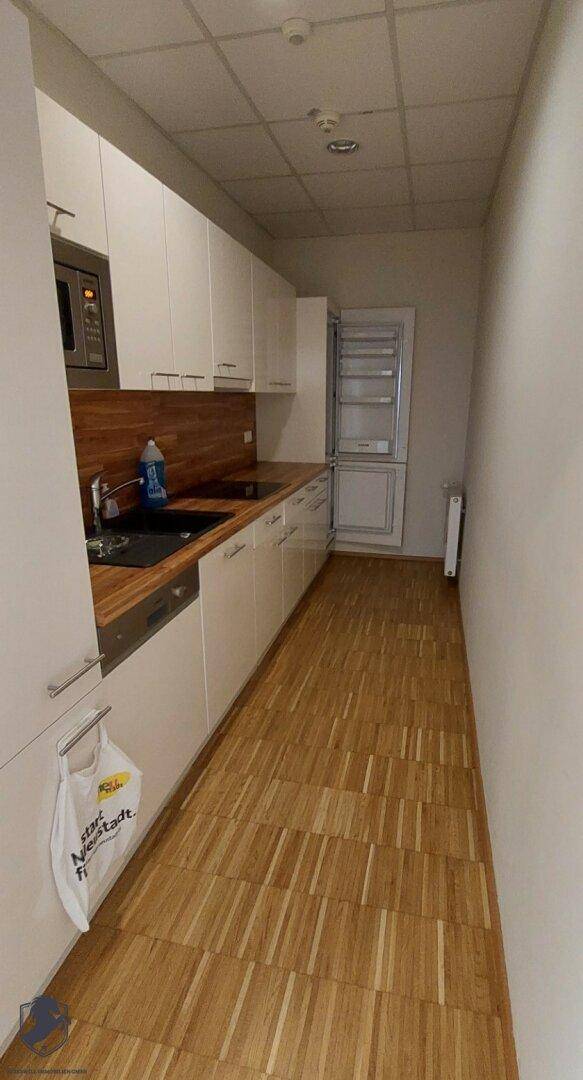 Schmale Küchenzeile mit weißen Schränken, Spüle und integriertem Kühlschrank.