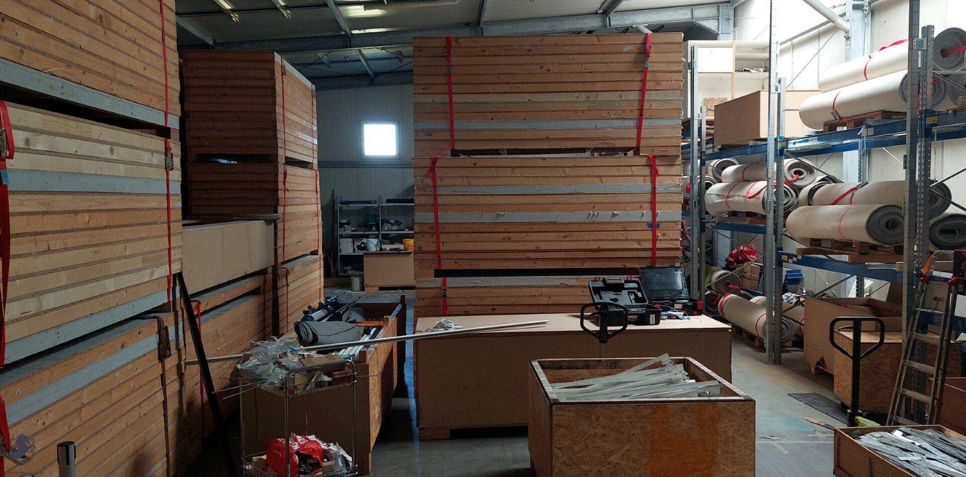 Lagerhalle mit gestapelten Holzkisten und Materialrollen auf Regalen, bereit zur Lagerung.