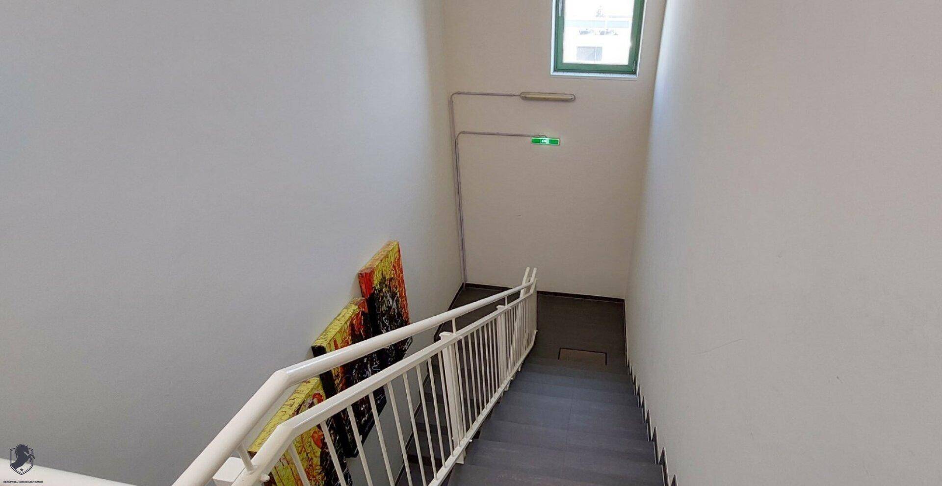 Treppenhaus mit weißem Geländer und farbenfrohen Kunstwerken an der Wand.