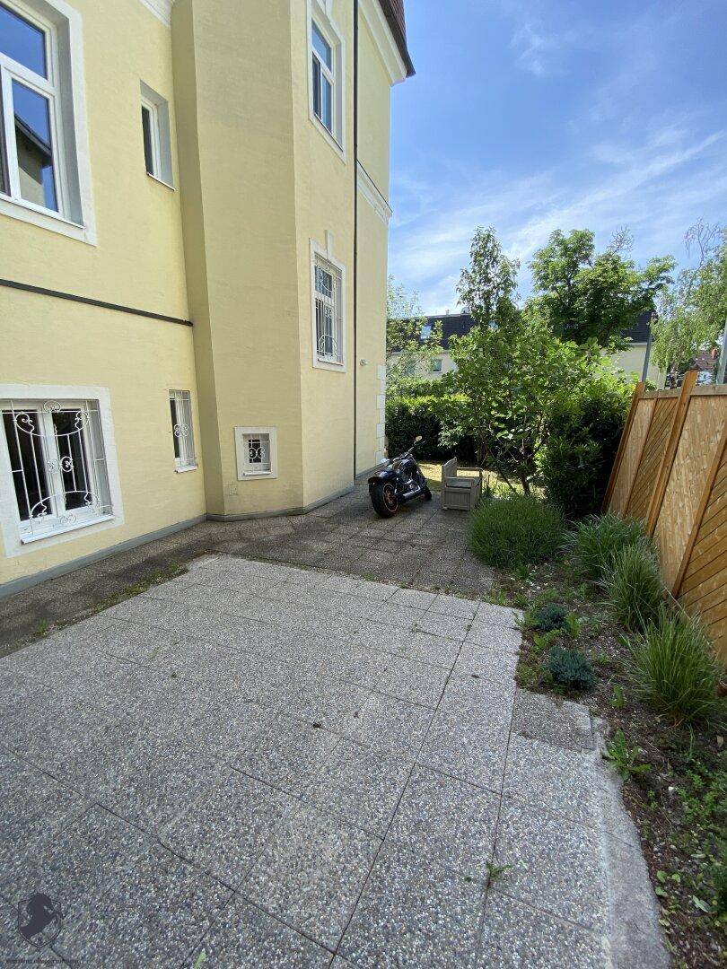 Gepflasterte Terrasse neben dem Gebäude mit Pflanzen und einem Motorrad im Freien.