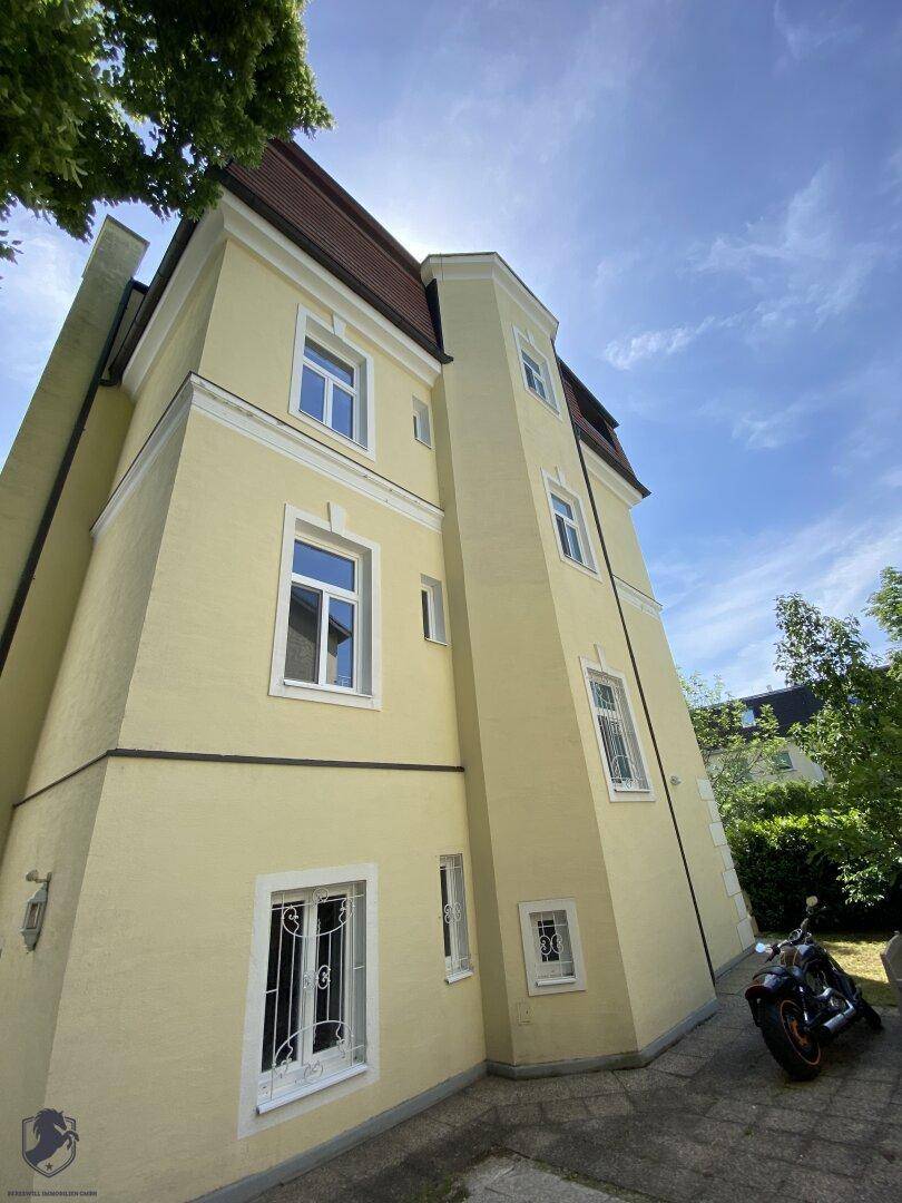 Eckansicht der gelben Villa mit Mansarddach und Fenstern unter blauem Himmel.