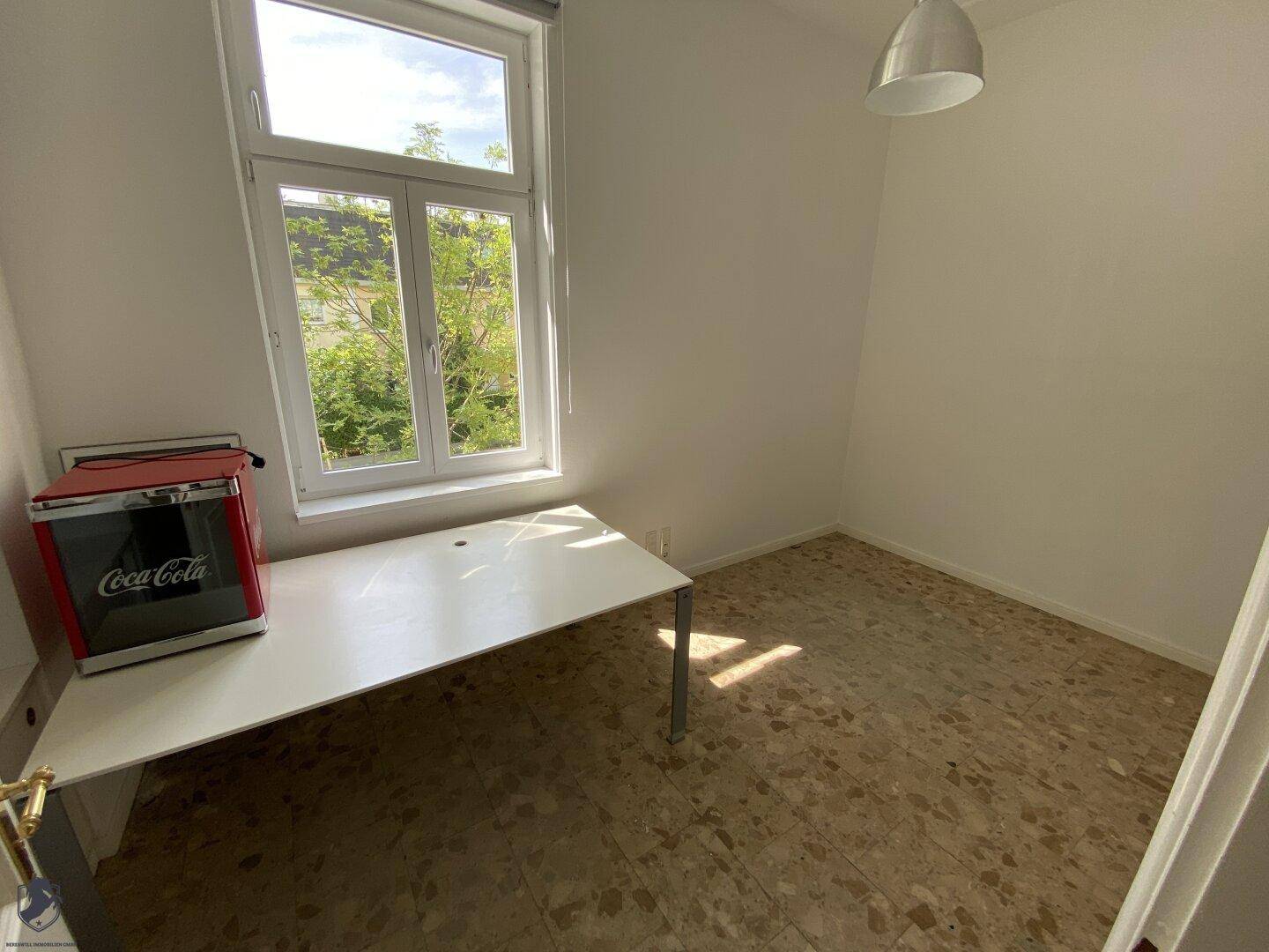 Kleiner Raum mit Terrazzoboden, Schreibtisch und großem Fenster mit viel Tageslicht.