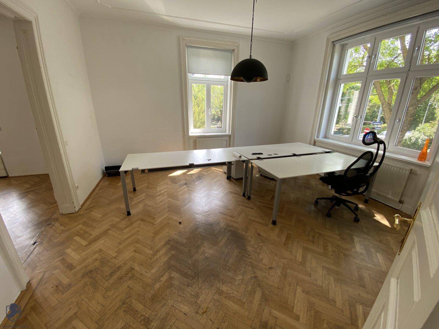 Geräumiges Büro mit Fischgrätparkett, großen Fenstern und Blick ins Grüne.