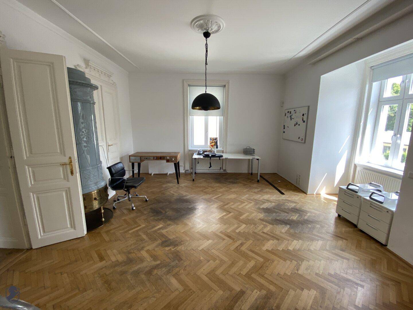 Helles Büro mit Fischgrätparkett, Stuckdecke und traditionellem Kachelofen.
