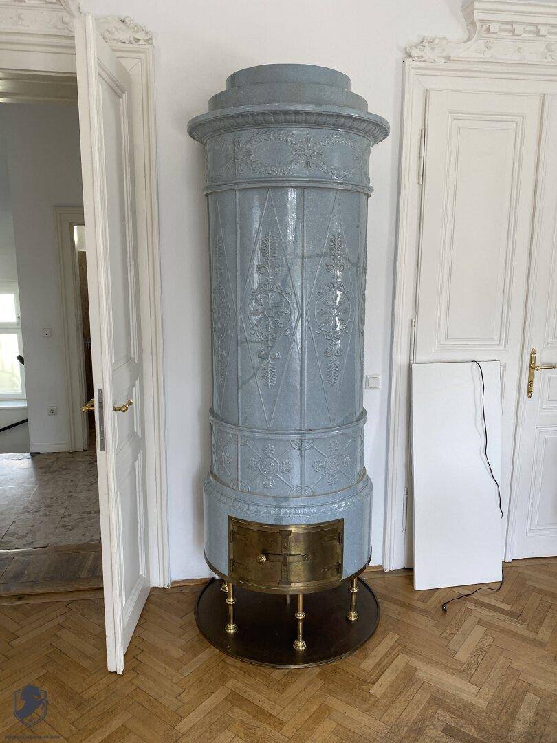 Detailaufnahme eines traditionellen blauen Kachelofens mit verzierten Elementen und Messingdetails.