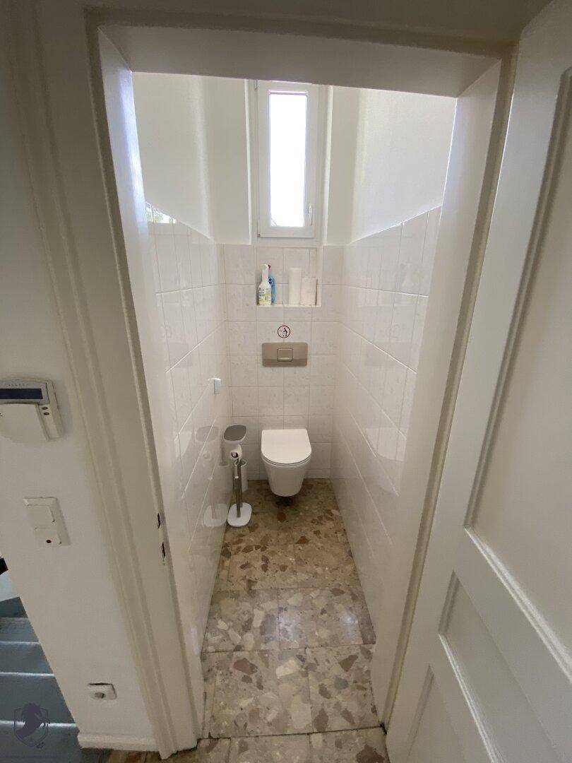 Modernes Gäste-WC mit wandhängender Toilette, kleinem Fenster und weißen Fliesen.