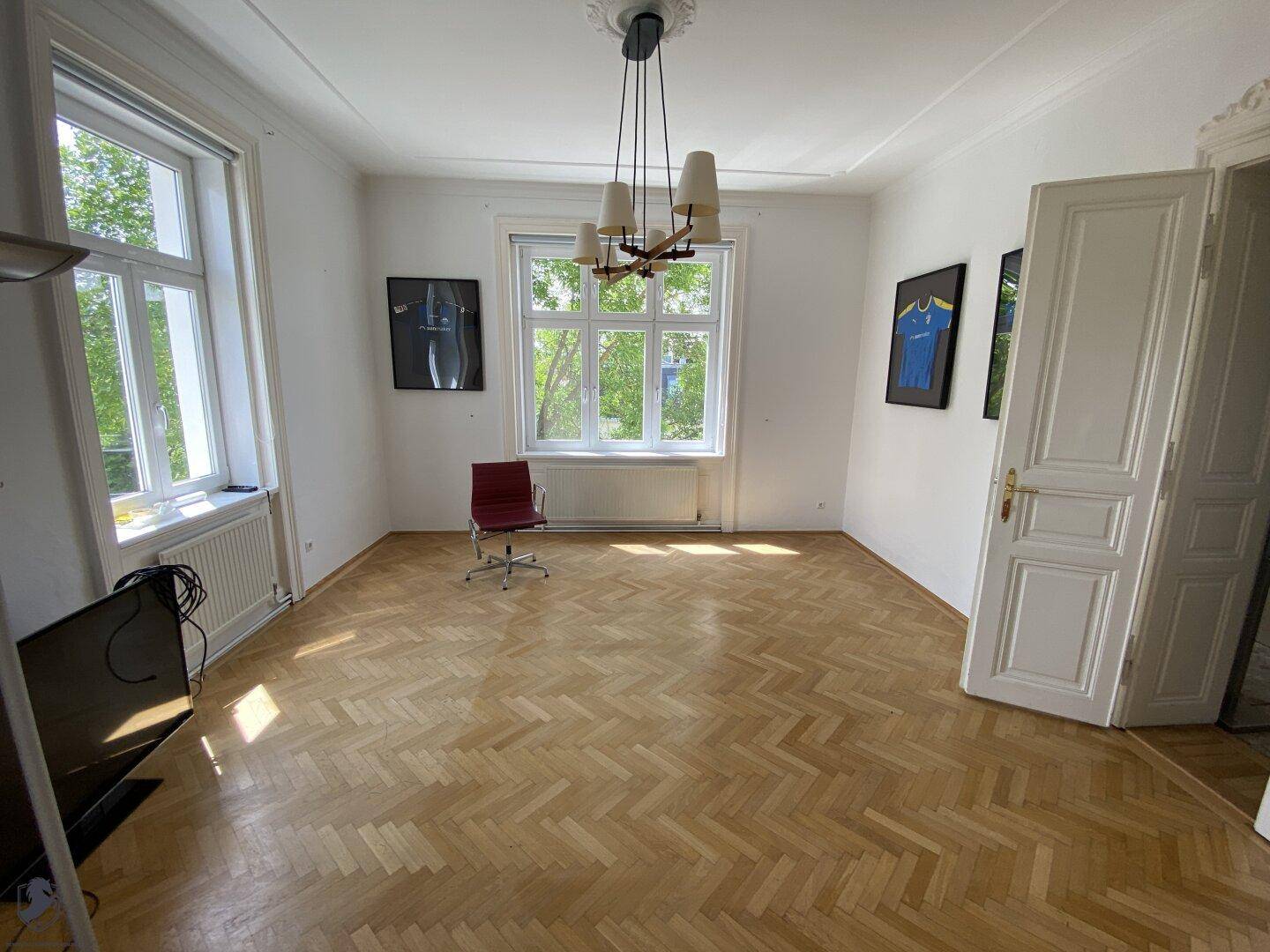 Heller Raum mit Fischgrätparkett, Stuckdecke und großen Fenstern, bietet viel Tageslicht.