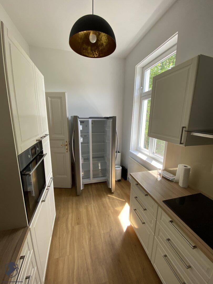 Moderne Küche mit weißen Schränken, Holz-Arbeitsplatte, Einbaugeräten und großem Fenster.