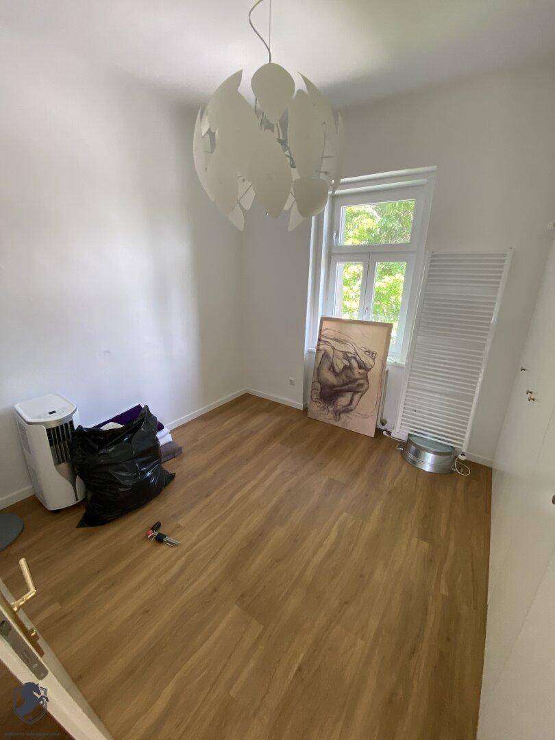 Heller Raum mit Laminatboden, großem Fenster und Heizkörper, derzeit unmöbliert.