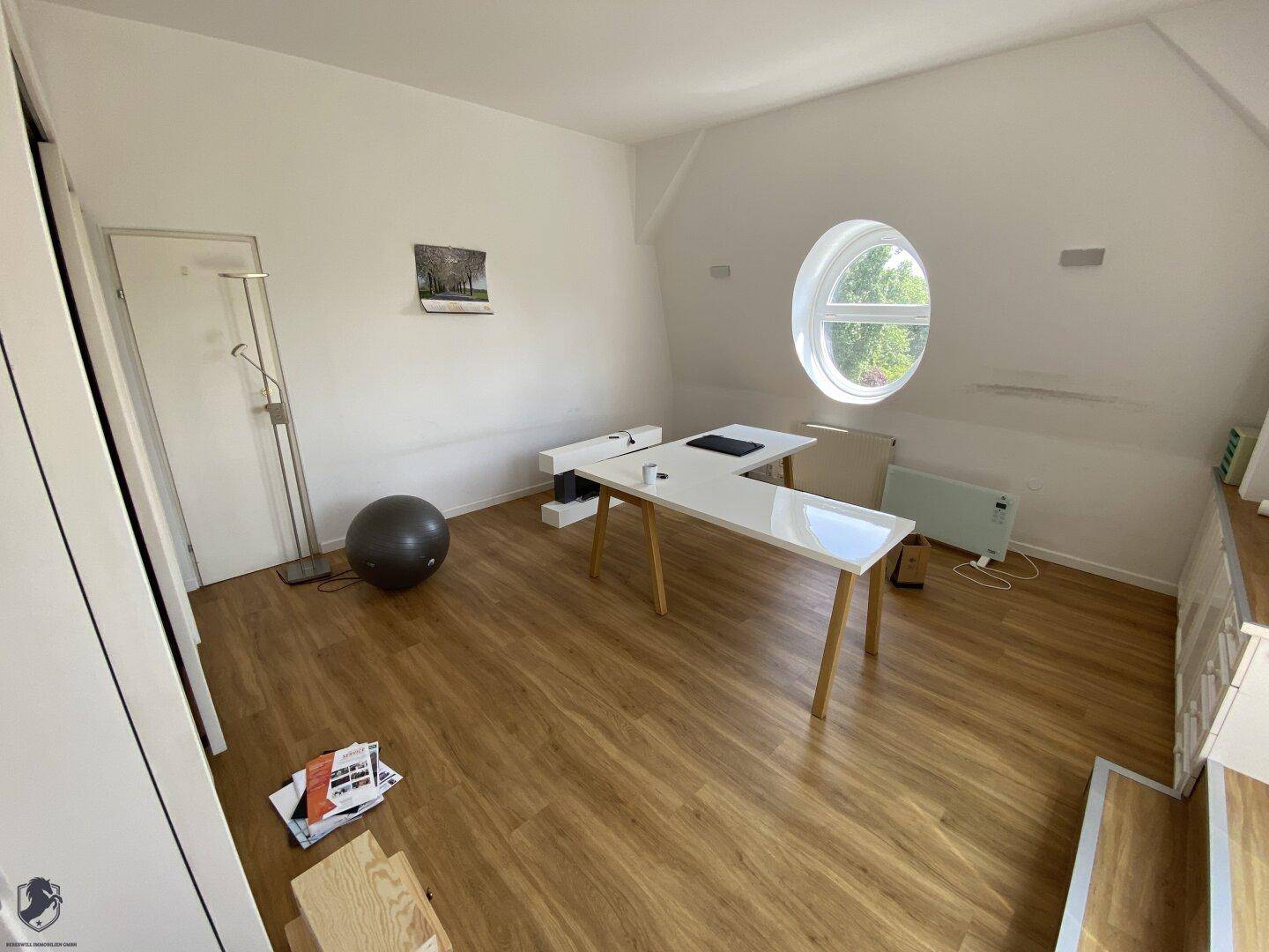 Dachgeschosszimmer mit Laminatboden, runden Fenstern und schrägen Wänden, ideal als Büro.