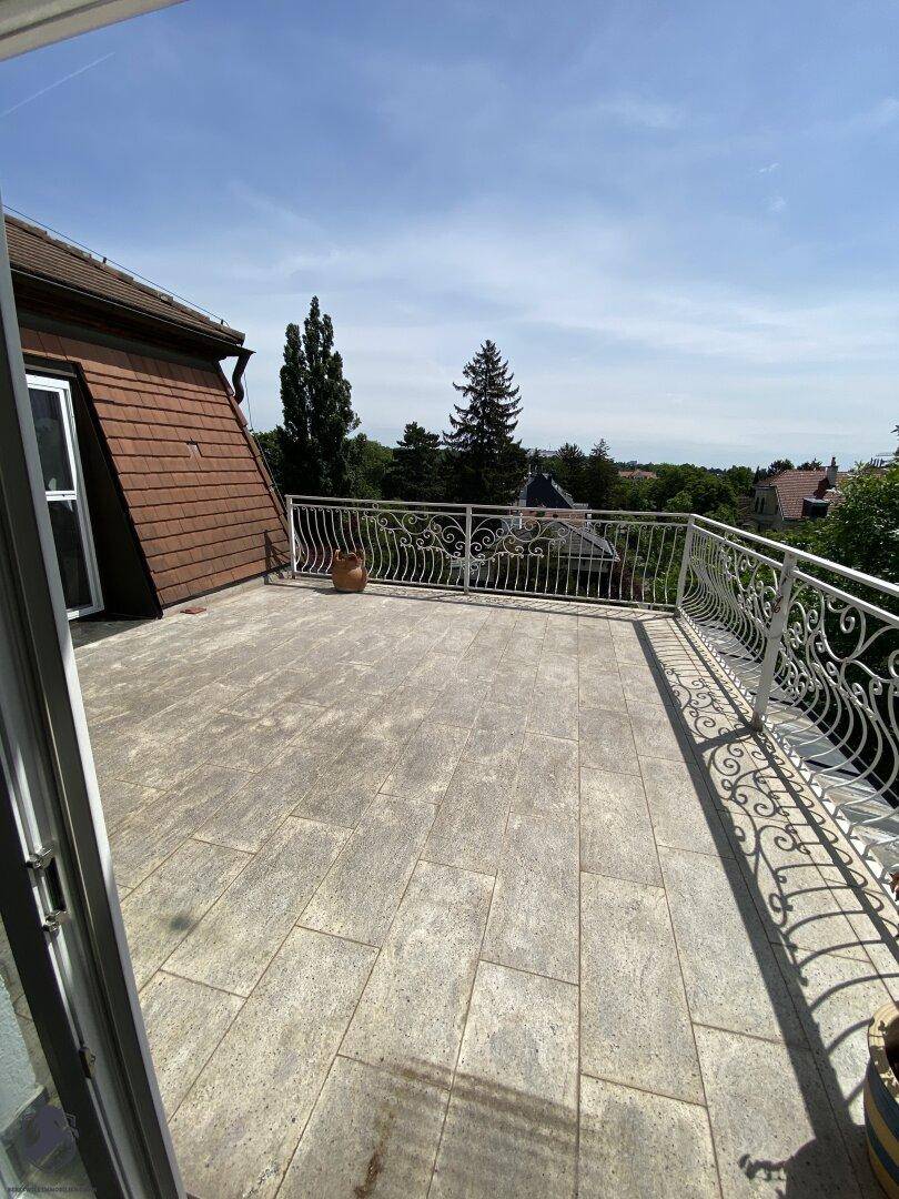 Große Dachterrasse mit Fliesenboden und schmiedeeisernem Geländer unter blauem Himmel.