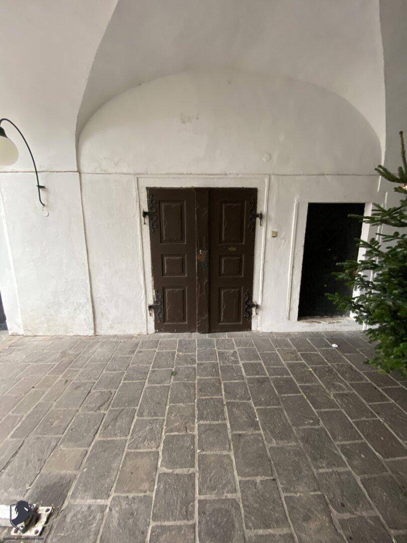 Historischer Durchgang mit gewölbter Decke, Steinboden und einer alten Holztür, geschmückt mit einem Weihnachtsbaum.
