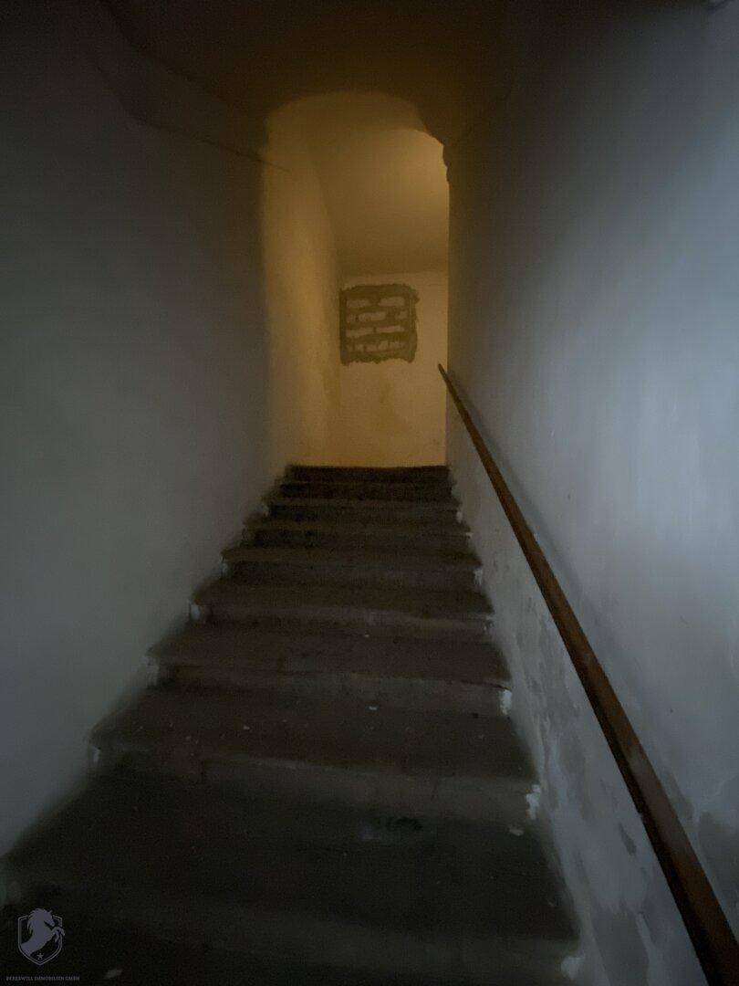 Dunkles Treppenhaus mit Steinstufen und einem einfachen Holzgeländer, das nach oben führt.