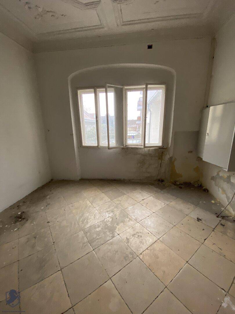Heller, unrenovierter Raum mit einem großen Fenster und Fliesenboden, der auf eine Modernisierung wartet.