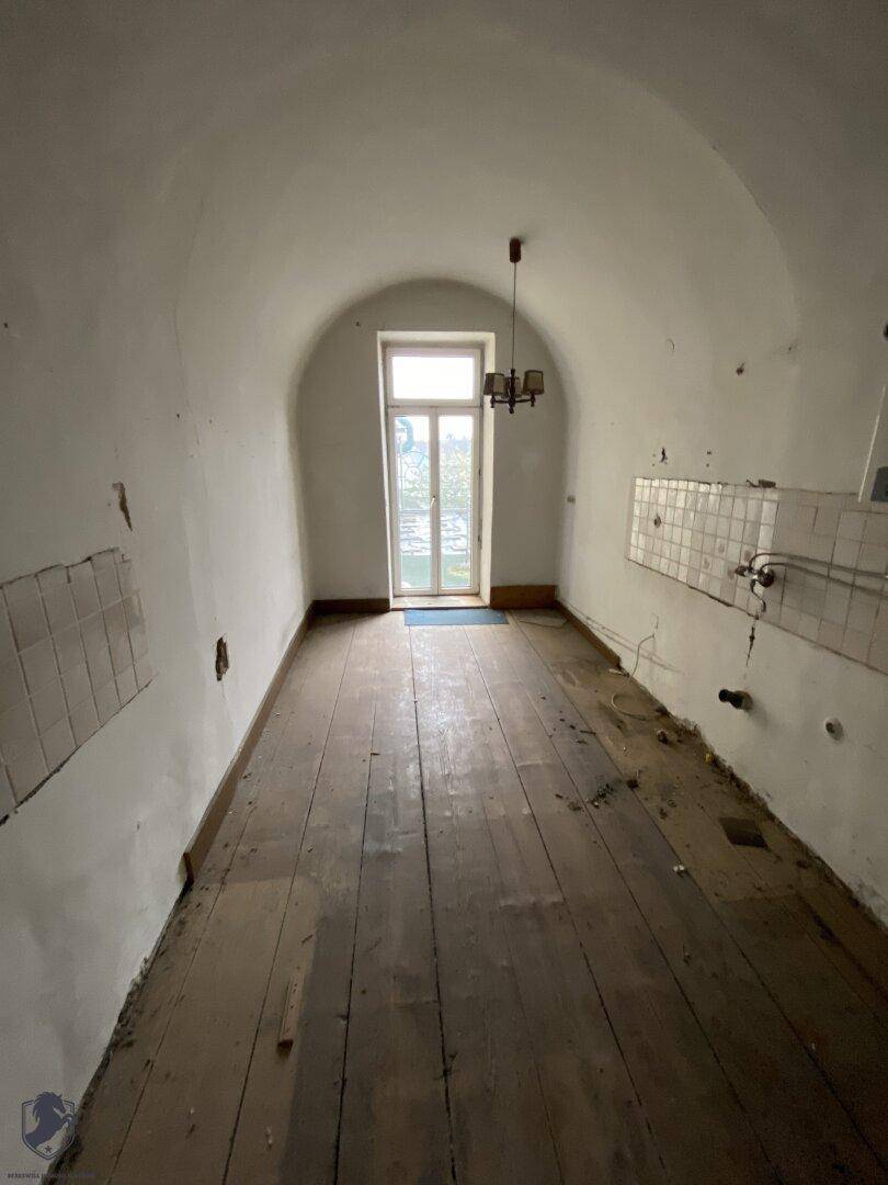 Langer Raum mit hoher Gewölbedecke, Holzdielenboden und einem Fenster am Ende, das Licht spendet.