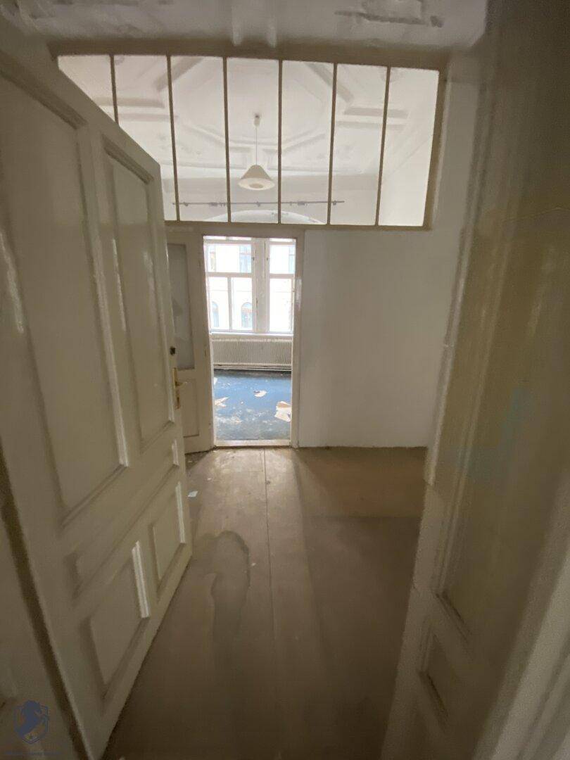 Durchgang zwischen Räumen mit Holzdielenboden und einem Fensterband über der Tür, das Licht hereinlässt.