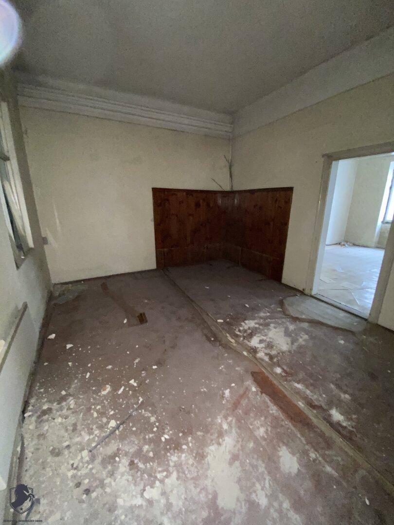 Dunkler, unrenovierter Raum mit beschädigtem Boden und einfacher Wandverkleidung, der eine Sanierung erfordert.